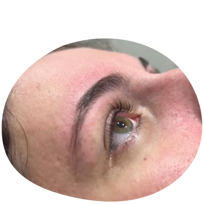 Close-up of a person's eye, showcasing natural eyelashes and well-groomed eyebrows, with a lightly flushed forehead.