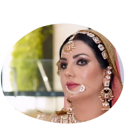 A bride adorned in elegant traditional jewelry and a richly embroidered lehenga, set against a softly blurred background.